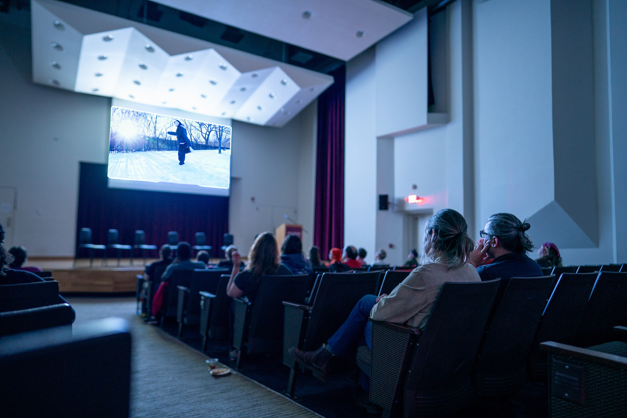Audience members view a film in an auditorium.